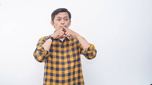 Asian man asking to be quiet with finger on lips against white background. Silence and secret concept