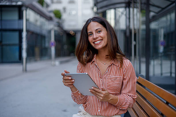 istock Businesswoman sitting on a bench, smiling while using a digital tablet, enjoying the vibrant city life in a modern urban setting 2230598551