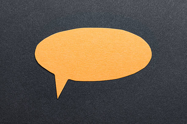 Orange cut out blank paper speech bubble of round shape with copy space for text on dark background, flat lay top view conceptual backdrop