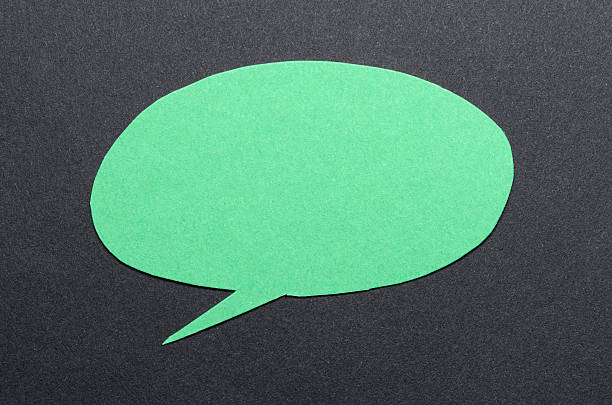 Green cut out blank paper speech bubble of round shape with copy space for text on dark background, flat lay top view conceptual backdrop