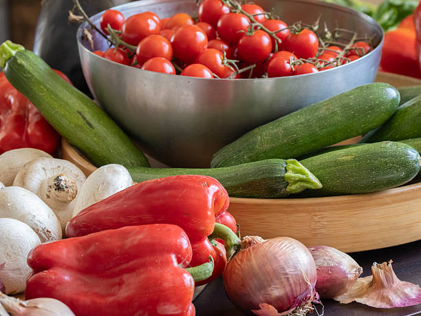 Assorted fresh vegetables including tomatoes, peppers, cucumber, and onions on a white plate, preparing for a healthy meal