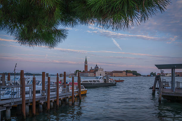 Sunset view of San Giorgio Maggiore Basilica and bell tower across the Venetian lagoon with boats and calm waves.