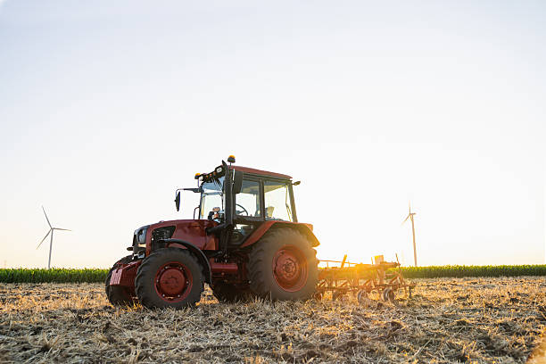 istock Agricultural tractor is working on the field with wind turbines. 2230620308