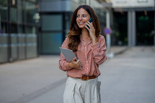 istock Professional woman talking on smartphone, walking downtown, carrying tablet, displaying confident demeanor 2230627730