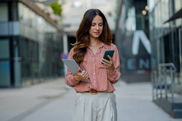 istock Professional female professional striding confidently downtown, checking digital devices during urban workday commute 2230627742