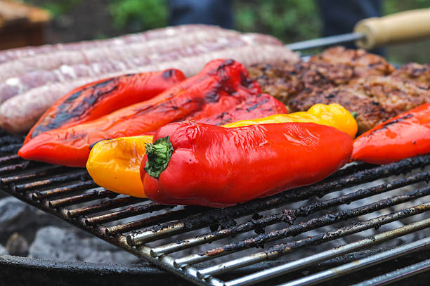 Seasonal red and yellow peppers fried on a grill with meat in the backyard of the house, close-up side view. Grill food concept.