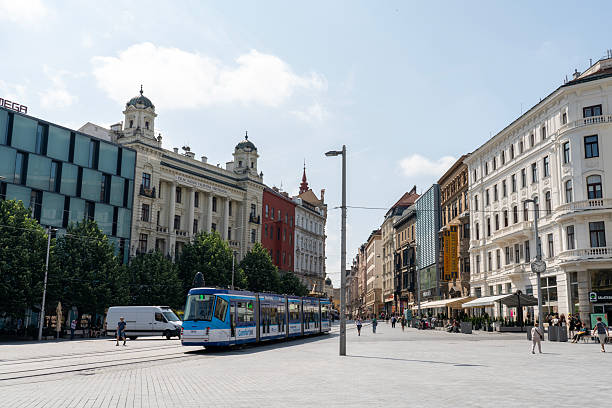 Czech Republic, Brno -  4. June 2025:  Town square and incidental people, tramway driving on traintrack against old city buildings. Sunny da.