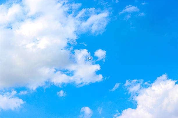 Background with clouds on blue sky. Sky view. Beautiful sunny sky. Clouds on blue sky. Sun shining through the puffy clouds. Airplane in the clouds.
