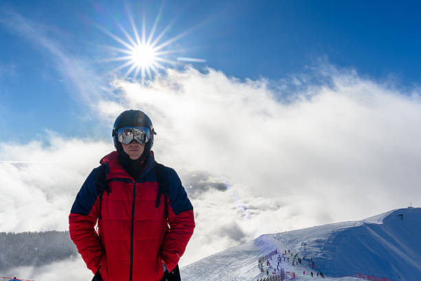 A skier poses on a snowy slope, with the sun shining brightly. The bright colors of the jacket contrast beautifully with the snowy background, showcasing the excitement of skiing.