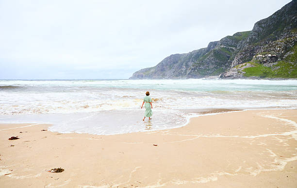 istock Young Woman Exploring a Scenic Beach With Rolling Waves and Coastal Cliffs 2230647496