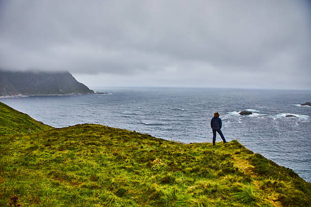 Solitary Figure Overlooking Vast Ocean on a Cloudy Cliffside Coastline