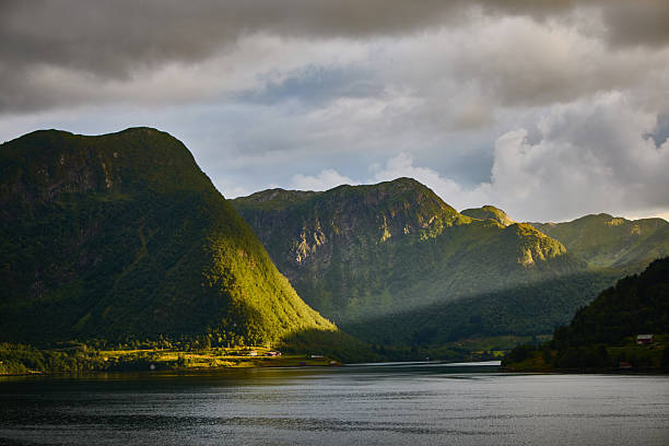 istock Sunlit Mountain Range Near a Calm Lake Under Dramatic Clouds 2230648208