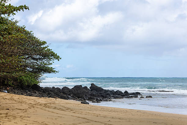 Turquoise waters surround the mountains in Hanalei Bay, Kauai, Hawaii.  Clouds expand and cover the mountain tops.