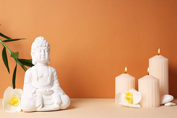istock Buddha statue, candles, flowers and stones on orange background, space for text 2230693058