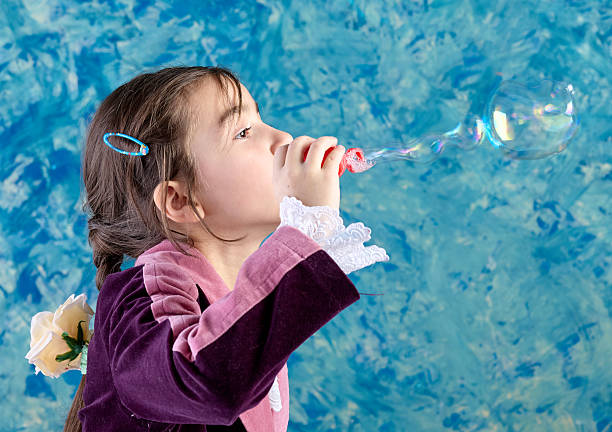 Cute elementary age girl is blowing bubbles. Studio shooting