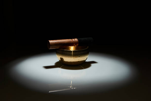 A brass singing bowl and striker under a spotlight on a black background. A dramatic, moody concept for sound therapy, mindfulness, yoga, spiritual rituals, and relaxation.