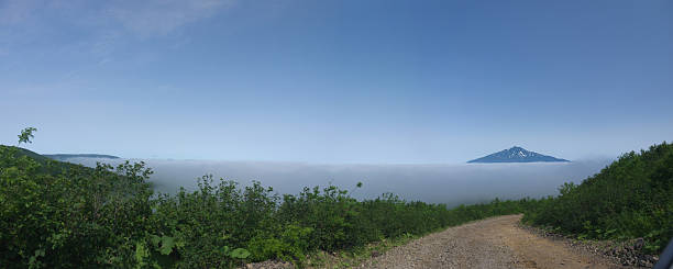 Driving by the mountain pass road with Bogdan Hmelniclky Volcano peak over the Stratus clouds on Iturup, panoramic view, Kuril islands