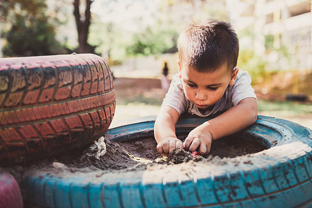 Young boy engrossed in playful exploration, digging in a sandbox made from repurposed tires, showcasing resourcefulness and childhood joy