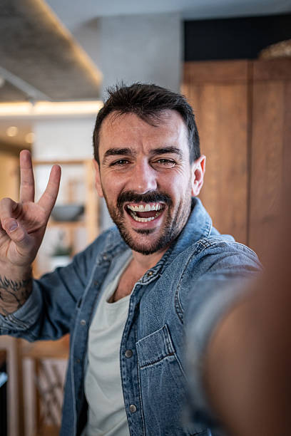 istock Happy man taking a selfie at home showing victory sign 2230722912