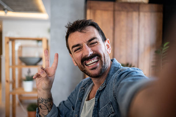 istock Happy man taking a selfie and making victory sign at home 2230722914