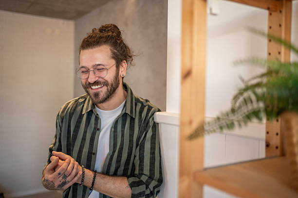 Young man wearing glasses smiling and leaning against a wall