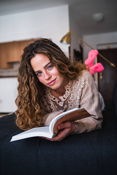 istock Young woman reading a book on the sofa at home 2230724419