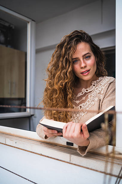 istock Young woman reading a book by the window 2230724544