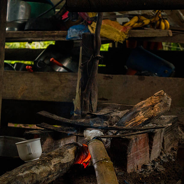 A rustic cooking area featuring a wood fire with a bamboo tube and utensils in the background, showcasing traditional culinary practices in Colombia.