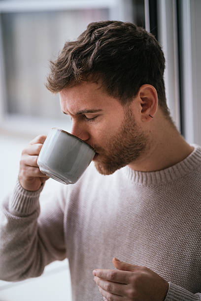 istock Young man drinking a cup of coffee by the window 2230726057