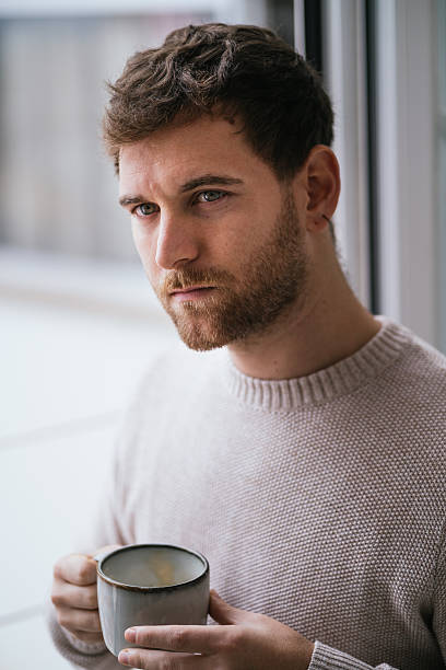 istock Thoughtful young man drinking a warm beverage by the window 2230726095