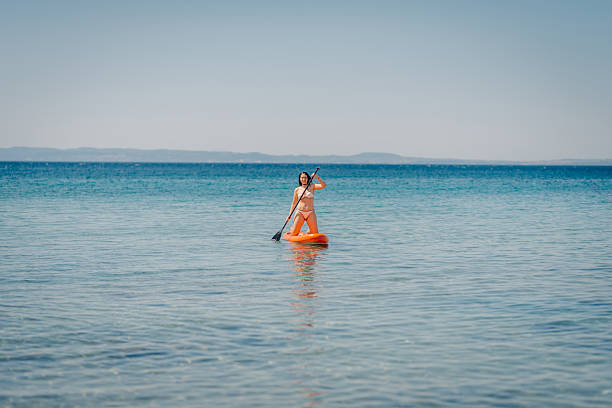 Young woman kneeling on a paddle board, enjoying a sunny day of paddleboarding on calm blue water