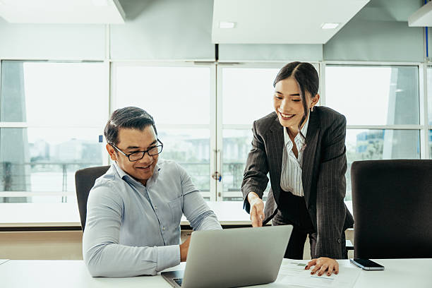 istock Two colleagues discussing a project at a modern office desk with a laptop and documents, looking engaged and cheerful 2230735127
