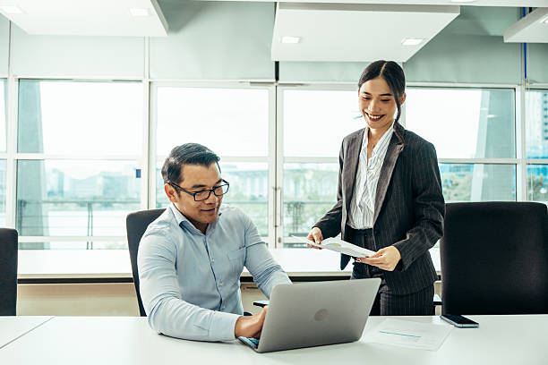 istock Two colleagues discussing a project at a modern office desk with a laptop and documents, looking engaged and cheerful 2230735143