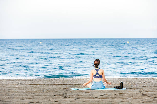 istock Woman practicing yoga in lotus pose on beach with ocean view 2230735912