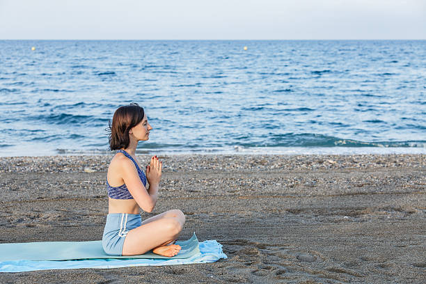 istock Woman practicing yoga on the beach in a seated meditation pose 2230736107
