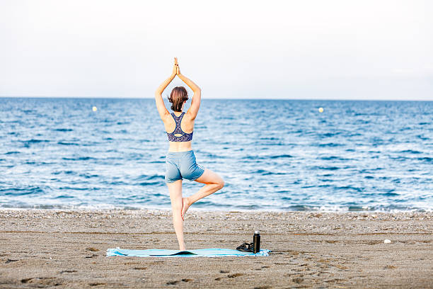 istock Woman practicing tree pose yoga on a beach near the ocean 2230736249