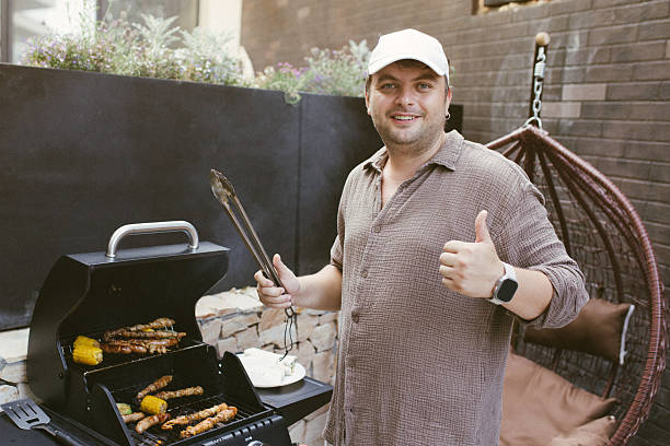 istock Man grilling sausages and corn on a gas barbecue 2230736507