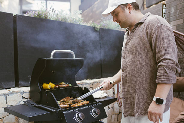 istock Man grilling sausages and corn on a gas barbecue 2230736653