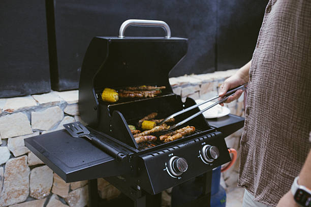 The image shows a grill with marinated meat, sausages, and grilled vegetables like zucchini and peppers, with the grill lid open and sunlight.