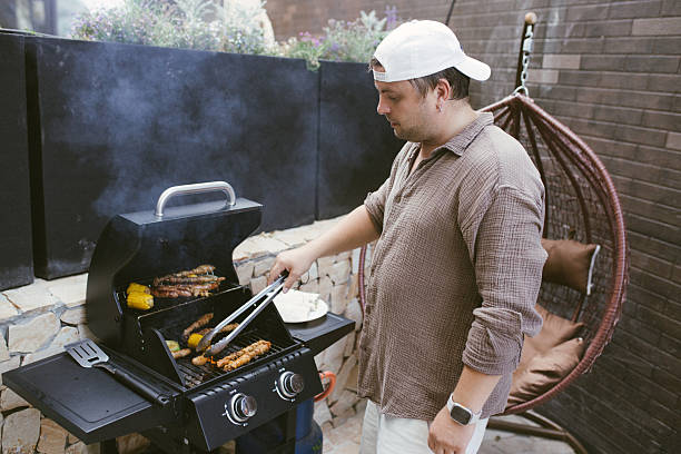 istock Man grilling sausages and corn on a gas barbecue 2230736816
