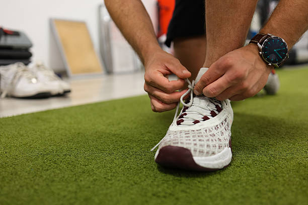 Close-up view of young man kneeling while tying shoeslaces in modern fitness gym.