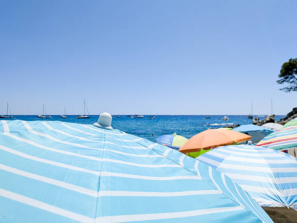 Colorful beach umbrellas lining the shore, offering shade and relaxation on a bright, sunny summer day by the tranquil Mediterranean Sea