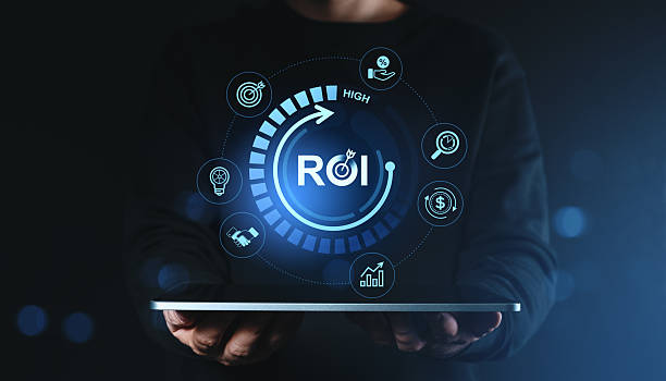 istock ROI return on investment concept with digital icons and growth analytics held above tablet by person in dark clothing on futuristic background. 2230743979