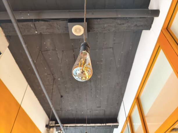 istock Close-up of a stylish, exposed lightbulb hanging from a dark ceiling. 2230744867