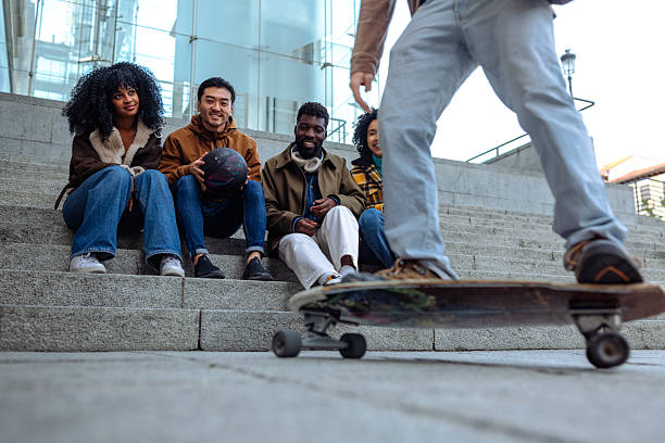 Low angle view of a skateboarder passing in front of four students sitting on some stairs