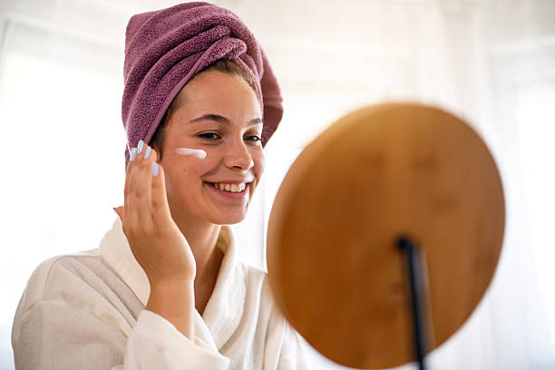 istock Young woman applying moisturizer while smiling in a relaxing morning routine 2230755681