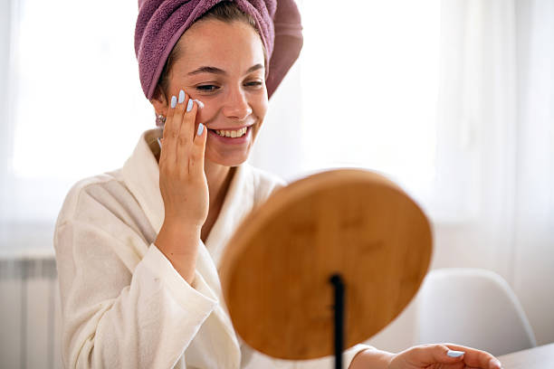 istock Young woman applying skincare in front of a mirror with a joyful expression 2230756021