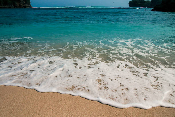 Close-up view of ocean waves with white foam gently washing onto the sandy beach at Gatra Beach, Malang, East Java, Indonesia. A tropical seascape symbolizing summer, travel, and relaxation by the sea.