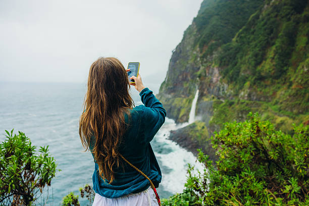 istock Woman Photographing Dramatic Oceanside Landscape with Waterfall on Madeira 2230757984