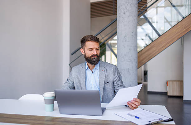 istock Businessman sitting at desk reading documents with laptop 2230758849